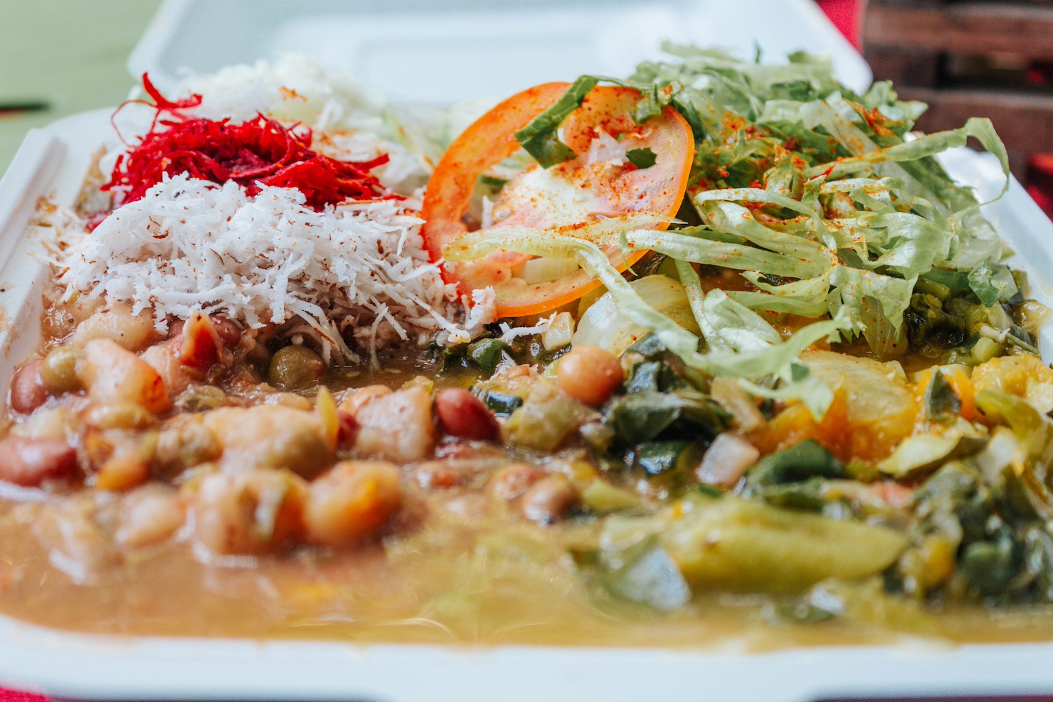 A plate of bean and pea stew, chickpea dumplings, banana, yam, stir-fried vegetables, grated beets and coconut. 
